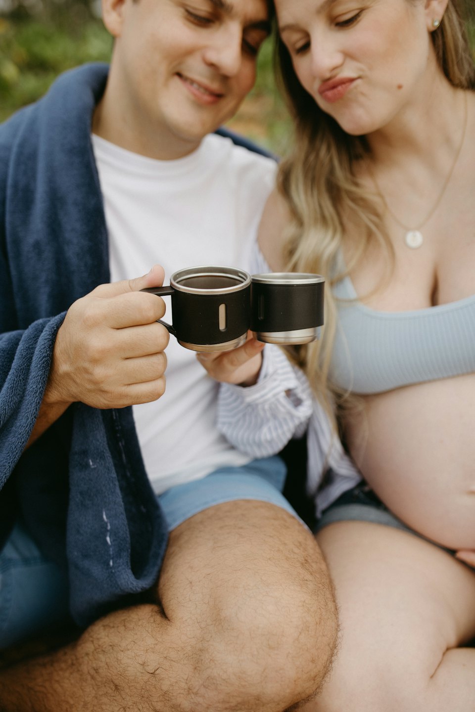 Ciężarna kobieta i jej partner stukają się kubkami podróżnymi na zewnątrz.