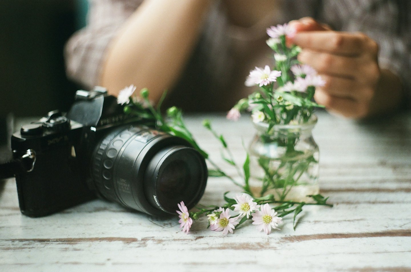 Stary aparat fotograficzny leży na stole obok kwiatowych aranżacji.